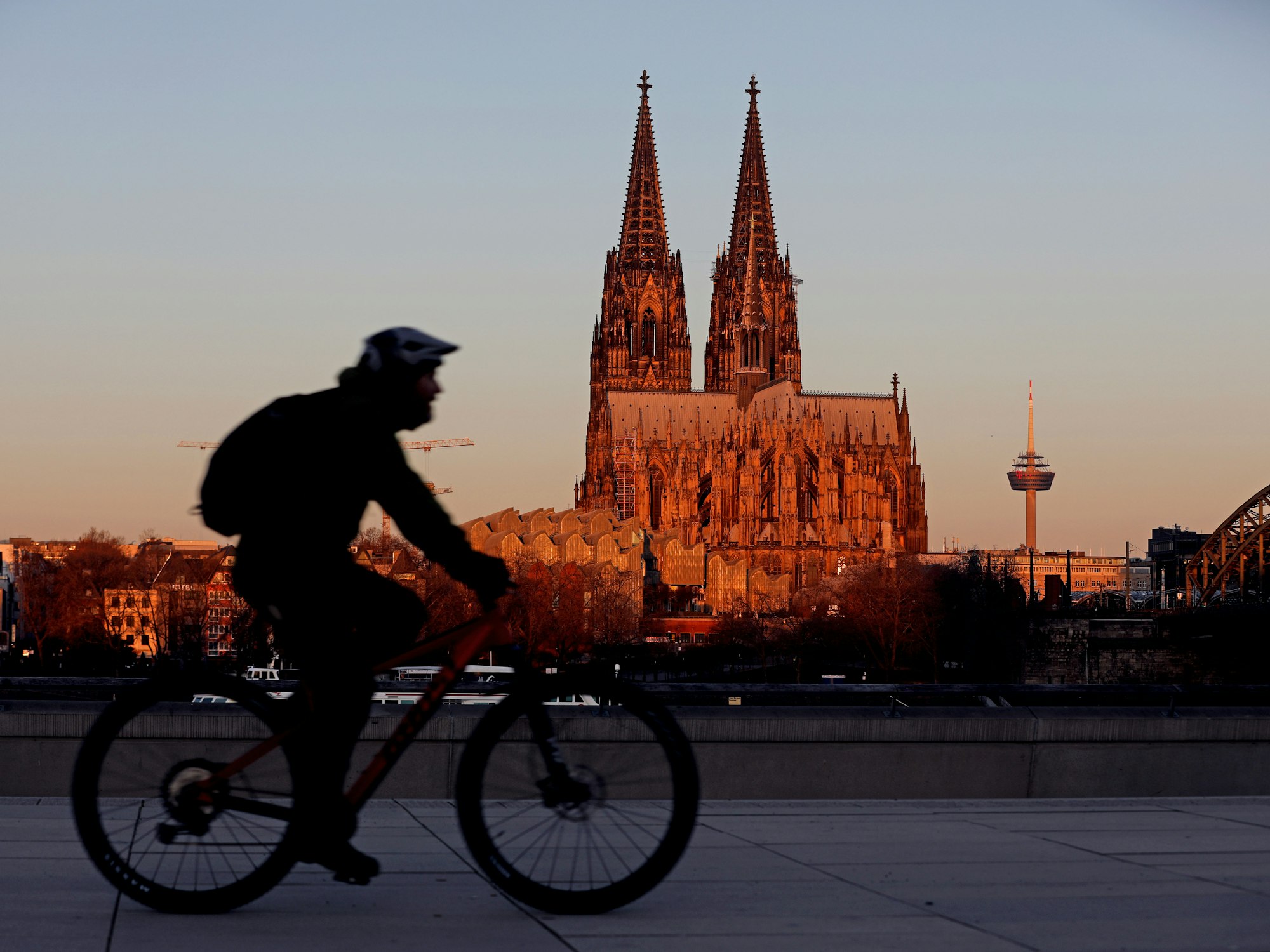 Ein Radfahrer fährt am Morgen am Dom vorbei, der von der aufgehenden Sonne angeleuchtet wird.