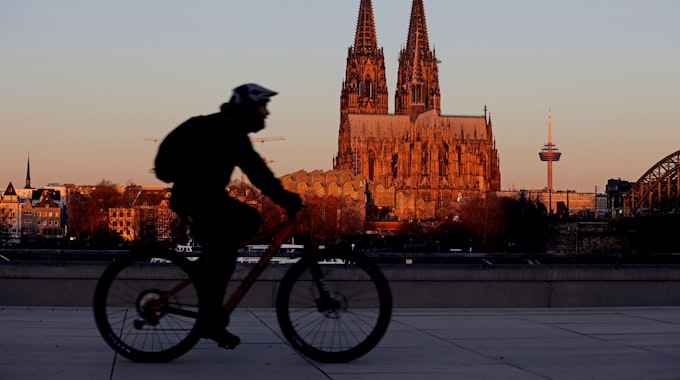 Ein Radfahrer fährt am Morgen am Dom vorbei, der von der aufgehenden Sonne angeleuchtet wird.