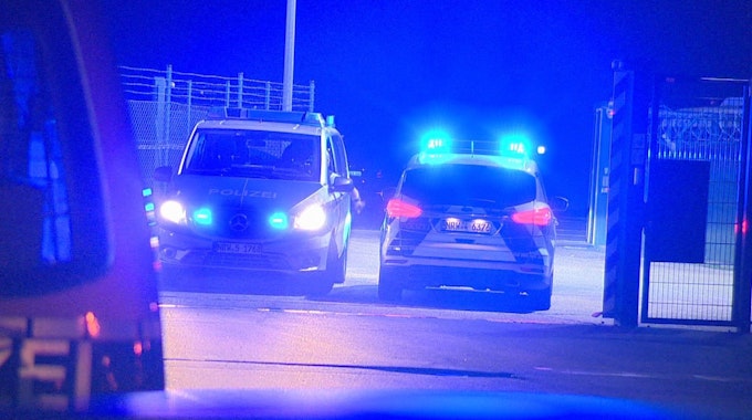 Polizisten passieren in Polizeifahrzeugen ein Tor am Flughafen Weeze, wo ein Auto einen Zaun an einer Rollbahn durchbrochen hat.