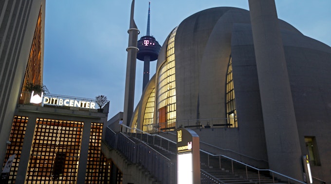 Die Moschee in Köln-Ehrenfeld ist am Morgen beleuchtet, dahinter ist der Kölner Fernsehturm zu sehen.