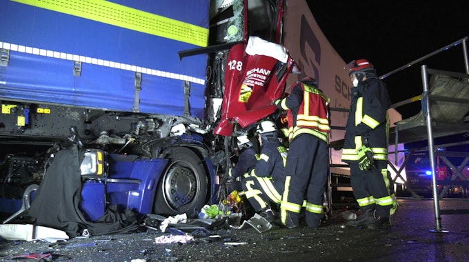 Einsatzkräfte der Feuerwehr untersuchen in der Nacht zum Mittwoch (13. Oktober 2021) die stark zerstörten Fahrerkabinen der verunfallten Lkw auf der A4.