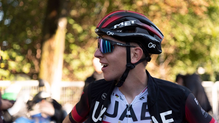 Tadej Pogacar lächelt nach einem langen Rennen. Auf seinem Kopf trägt er einen Helm. Außerdem trägt er eine Sonnenbrille.