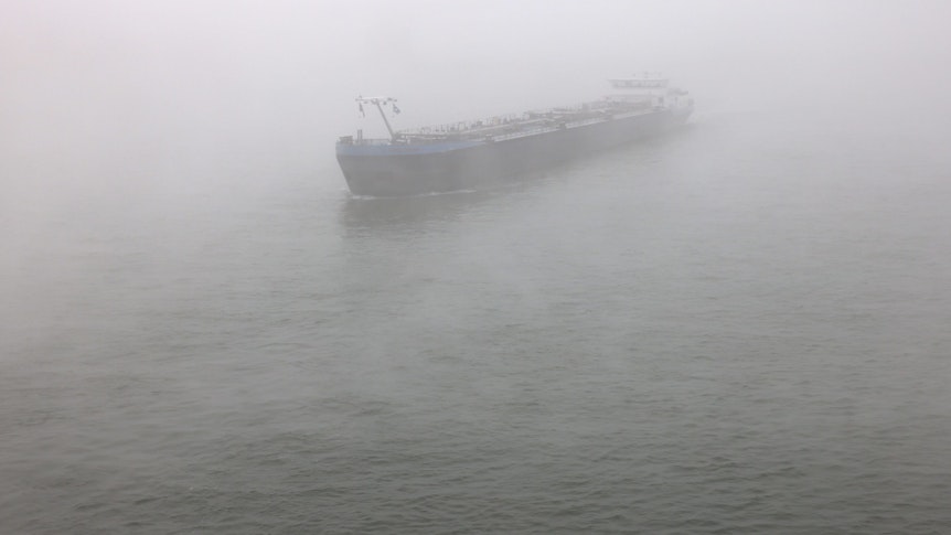 Ein Schiff fährt im Nebel über den Rhein.