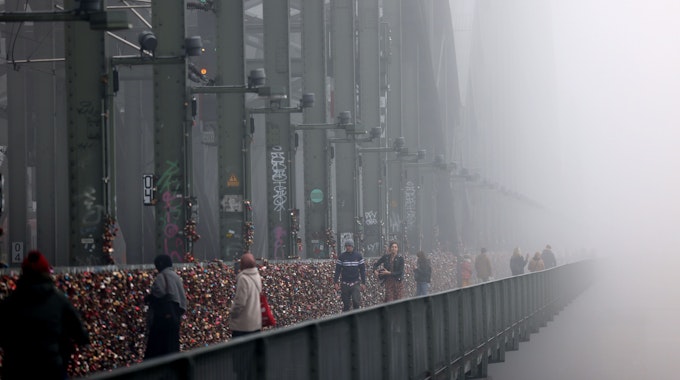 Spaziergänger gehen im Nebel über die Hohenzollernbrücke.