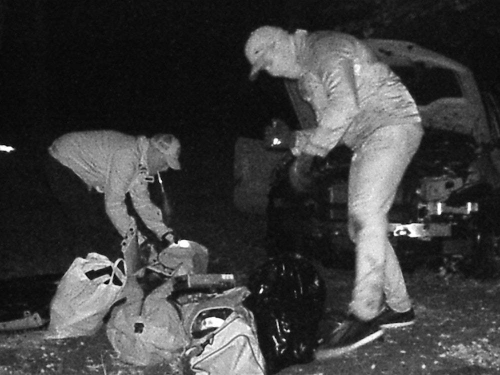 Auf dem Bild der Wildkamera sieht man, wie Unbekannte bei Nacht Einzelteile des ausgeschlachteten BMW in Taschen verstauen.