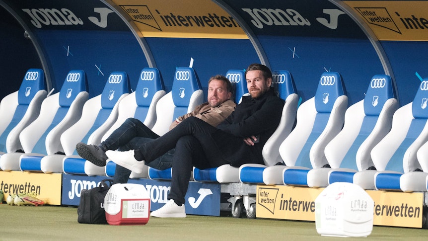 Thomas Kessler und Jörg Jakobs sitzen bei der Partie TSG Hoffenheim gegen 1. FC Köln auf der Bank.