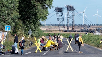 Bei der Aktion „Platz nehmen für Lützerath“ sitzen Teilnehmer mit Stühlen und Tischen im Ort Lützerath auf der Straße am Tagebaurand.