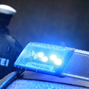 Ein Polizist steht am 15. März 2019 im Regen vor einem Streifenwagen, dessen Blaulicht aktiviert ist.