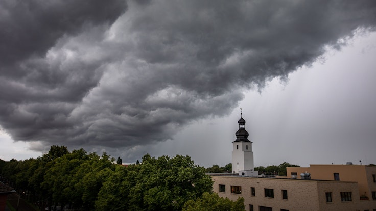 Dunkle Wolken ziehen am 4. Juli 2021 kurz vor einem Gewitter mit Starkregen über den Kölner Ortsteil Sülz. Der Kirchturm rechts gehört zur Kirche „Zur heiligen Familie“.