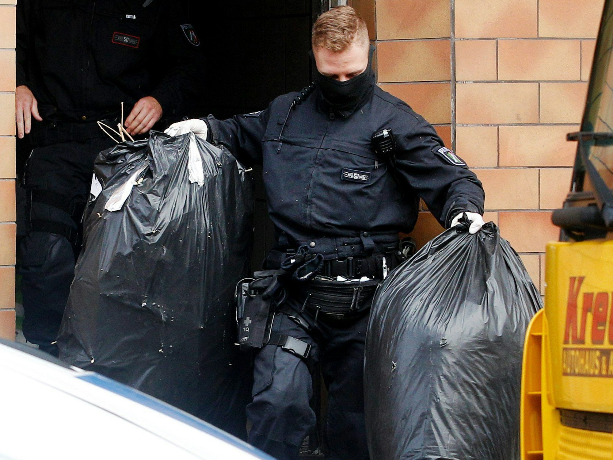 Ein Polizist trägt zwei Säcke mit den Resten von Cannabis-Pflanzen aus einem Haus.