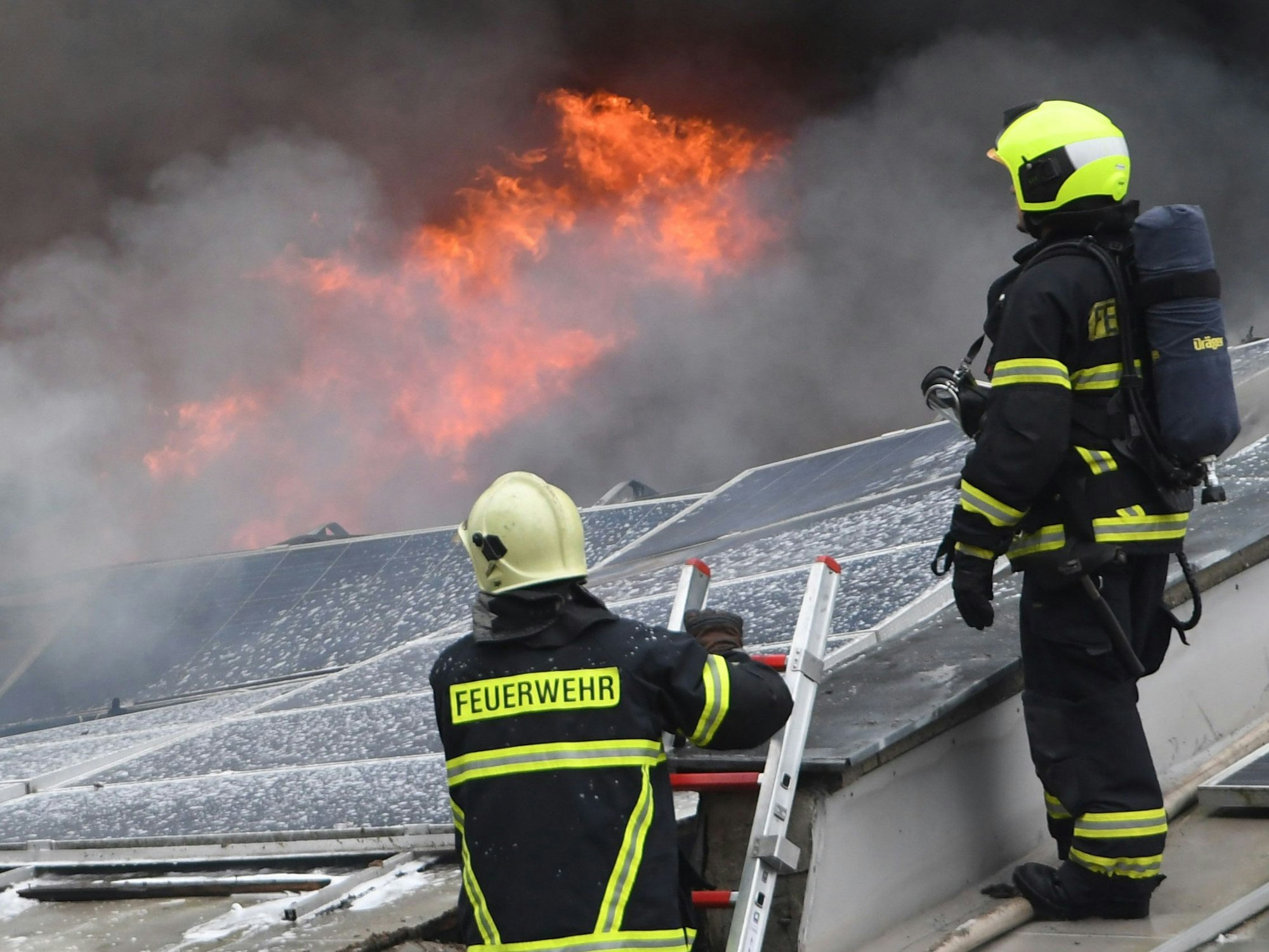 Feuerwehrleute stehen auf dem Dach eines brennenden Gebäudes.