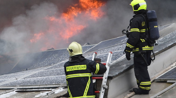 Feuerwehrleute stehen auf dem Dach eines brennenden Gebäudes.&nbsp;