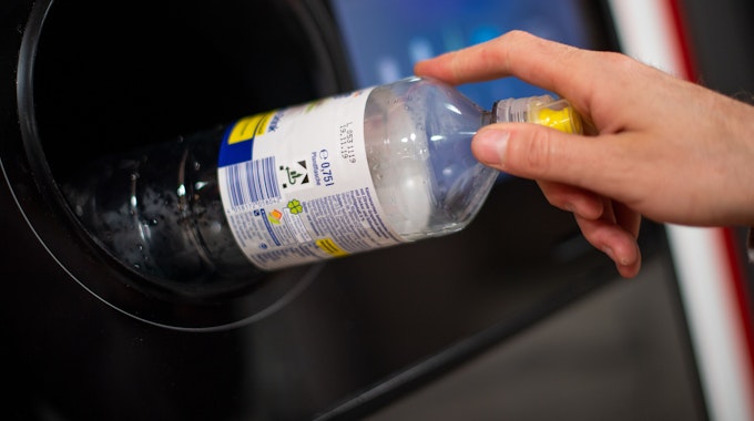 Ein Mann steckt eine Pfandflasche in einen Pfandflaschenautomaten in einem Supermarkt.