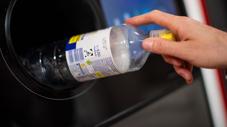 Ein Mann steckt eine Pfandflasche in einen Pfandflaschenautomaten in einem Supermarkt.