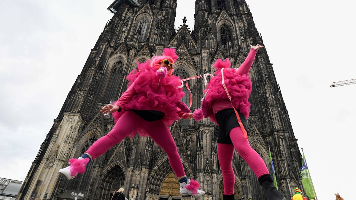 Verkleidete Frauen springen vor dem Kölner Dom in die Höhe. Die Weiberfastnacht leitet den Beginn des Straßenkarnevals ein.