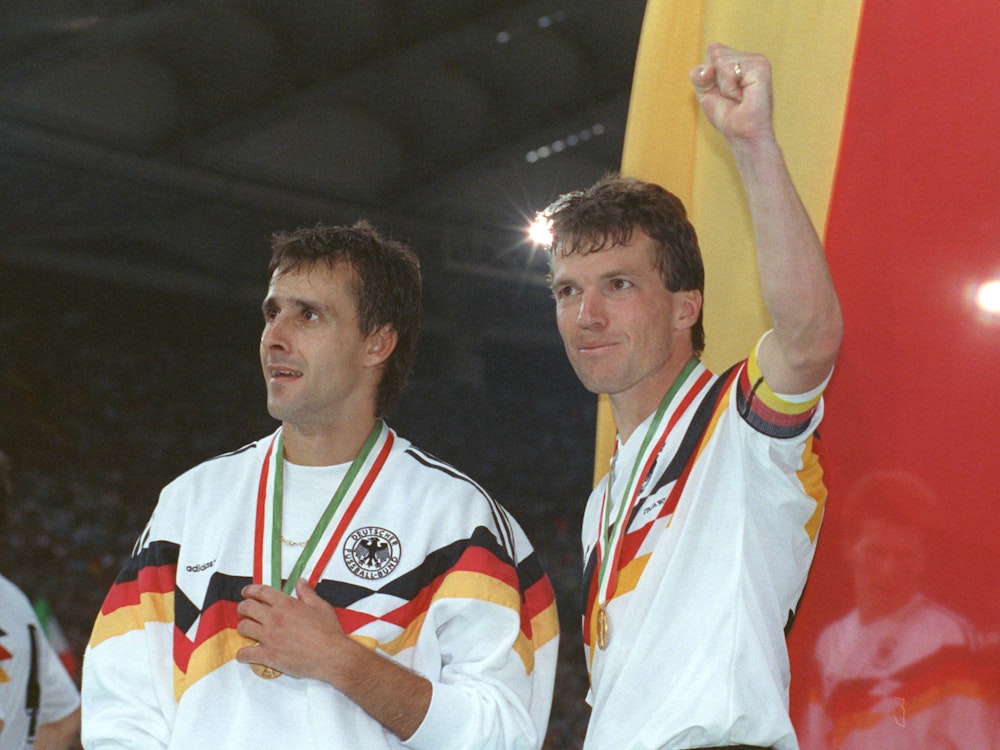 Der deutsche Mittelfeldspieler und Kapitän Lothar Matthäus (r) und sein Mitstreiter Pierre Littbarski (l) bejubeln vor der deutschen Fahne den WM-Titel.