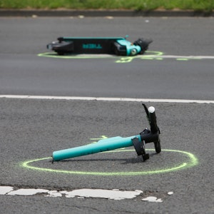 Ein in zwei Teile gerissener E-Scooter liegt auf einer Straße. Die Polizei hat beide Stelle mit Farbe markiert.