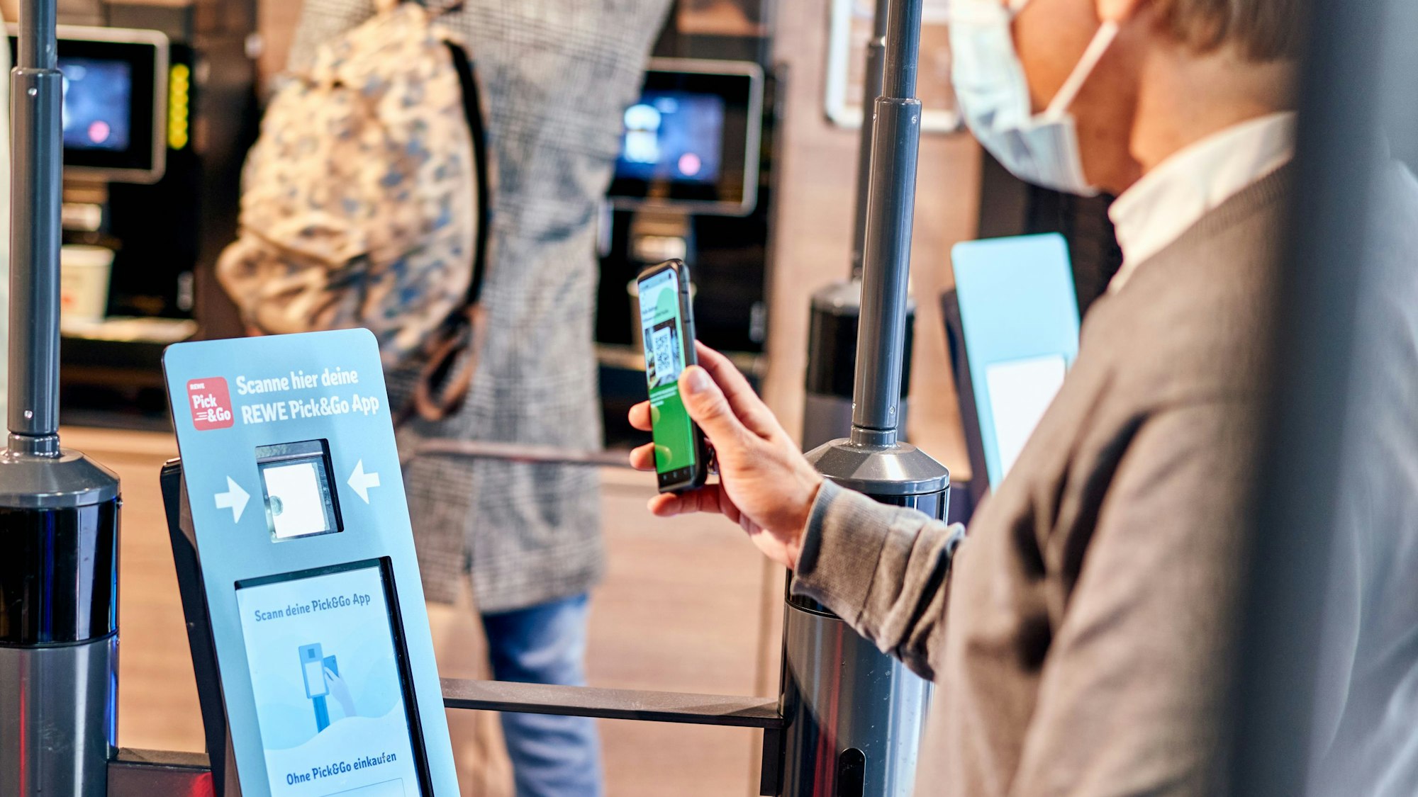Hybrides Einkaufen bei Rewe: Ein Mann meldet sich am Eingang über einen QR-Code mitder Scan&Go-App an.