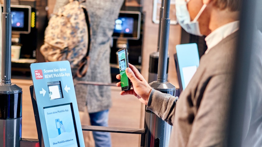 Hybrides Einkaufen bei Rewe: Ein Mann meldet sich am Eingang über einen QR-Code mit der Scan&Go-App an.