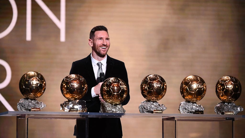 Lionel Messi steht vor einem Tisch mit dem sechsmal gewonnen Ballon d'Or.