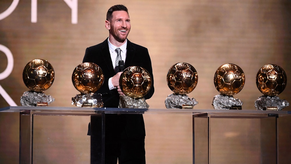 Lionel Messi steht vor einem Tisch mit dem sechsmal gewonnen Ballon d'Or.