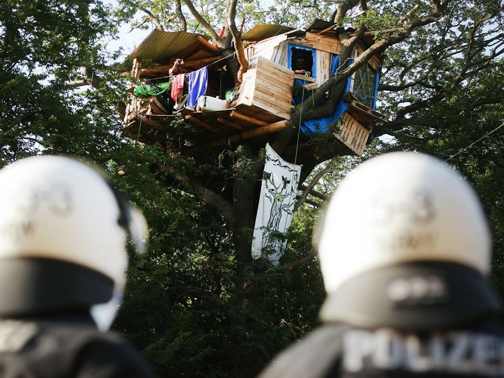 Am 23.06.2020 stehen zwei Polizisten am Fuße eines Baumes, in dem Aktivisten ein Haus im Hambacher Forst gebaut haben.