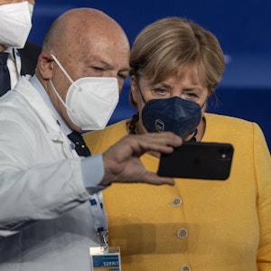 Ein Mitarbeiter des Gesundheitswesens macht ein Selfie mit der geschäftsführenden Bundeskanzlerin Angela Merkel (CDU,r) während sie sich für ein gemeinsames Gruppenfoto aufstellen.