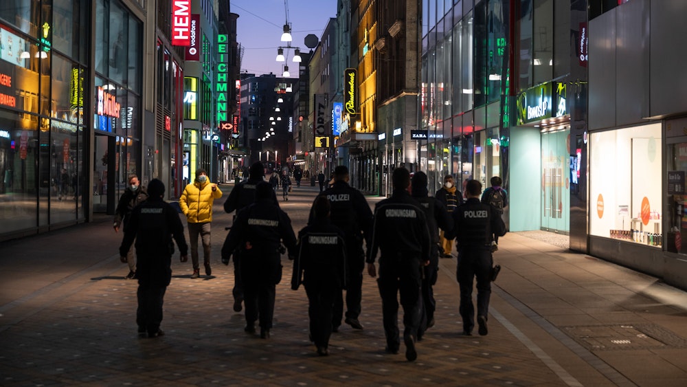 Mitarbeiter von Polizei und Ordnungsamt kontrollieren in der Abenddämmerung in der Fußgängerzone.