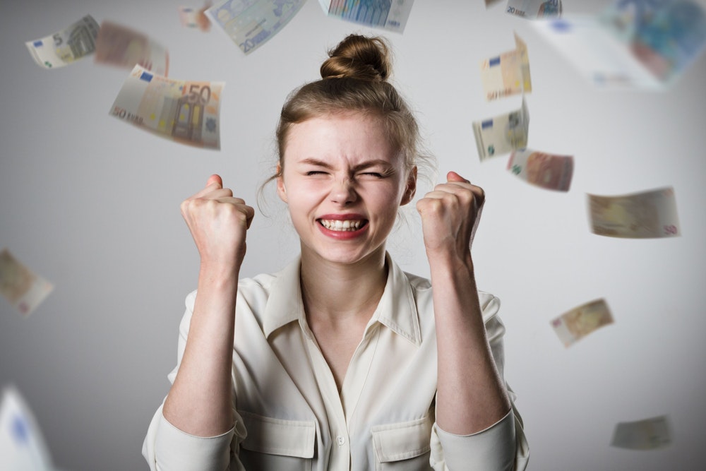 Junge Frau freut sich, während sie in einem Regen aus Euro-Geldscheinen steht. Bild zum Artikel Lotto Millionenkracher 2021 bei Westlotto.