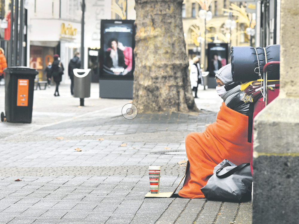 Eine obdachlose Person sitzt am Straßenrand.