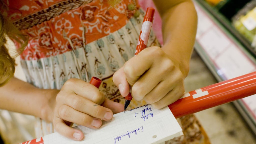 ARCHIV - Ein linkshändiges Mädchen kauft mit einem Einkaufszettel in einem Supermarkt ein und hakt mit einem Stift die Waren ab.&nbsp;