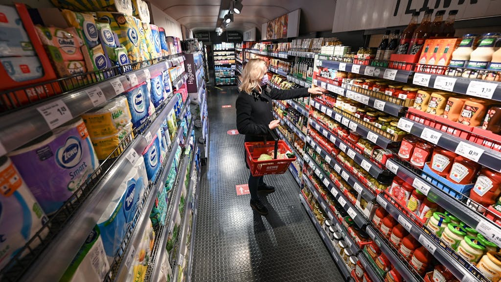Eine Frau steht bei der Vorstellung des temporären Projekts "Fairer Supermarkt im Zug" im Frankfurter Hauptbahnhof mit einem Einkaufskorb vor einem Lebensmittelregal.&nbsp;