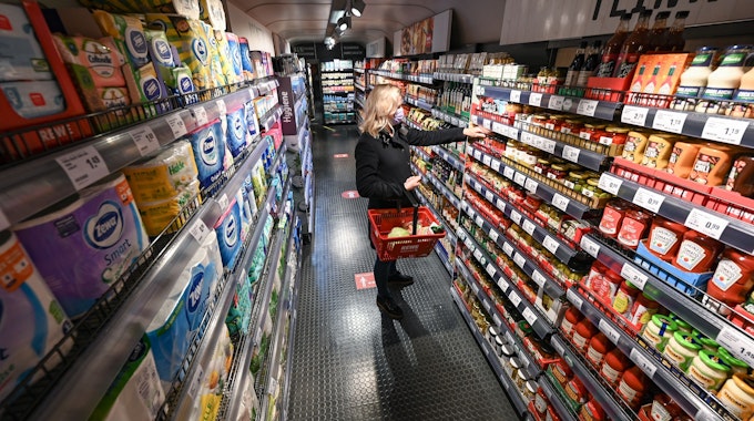Eine Frau steht bei der Vorstellung des temporären Projekts "Fairer Supermarkt im Zug" im Frankfurter Hauptbahnhof mit einem Einkaufskorb vor einem Lebensmittelregal.