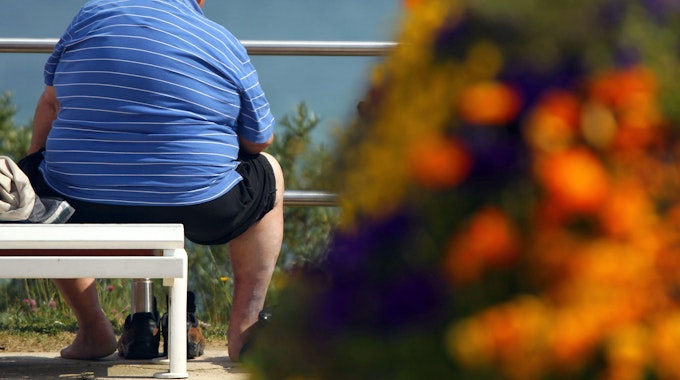 Ein übergewichtiger Mann sitzt auf einer Bank an der Strandpromenade an der Ostsee. Immer mehr Menschen in Deutschland sind einer Studie zufolge fettleibig.