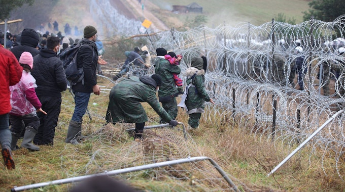 Migranten, die in Belarus vor der Grenze zu Polen festsitzen, stehen am 8. November vor Stacheldraht, auf der anderen Seite stehen Soldaten.