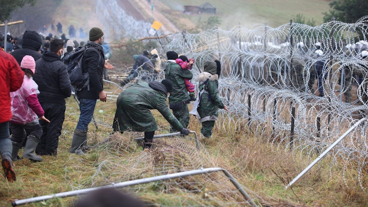 Migranten, die in Belarus vor der Grenze zu Polen festsitzen, stehen am 8. November vor Stacheldraht, auf der anderen Seite stehen Soldaten.
