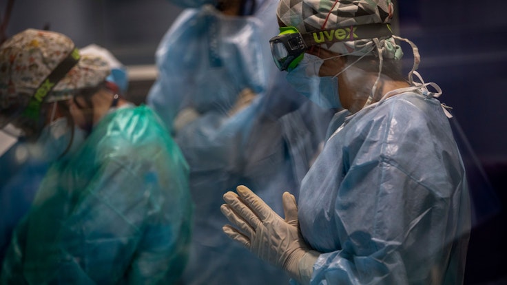 Ein Mitarbeiter des Gesundheitswesens mit doppelter Maske und einer Uvex-Brille schaut zu, wie ein Team bei einem Covid-19-Patienten auf der Intensivstation des Hospital del Mar einen Luftröhrenschnitt durchführt.