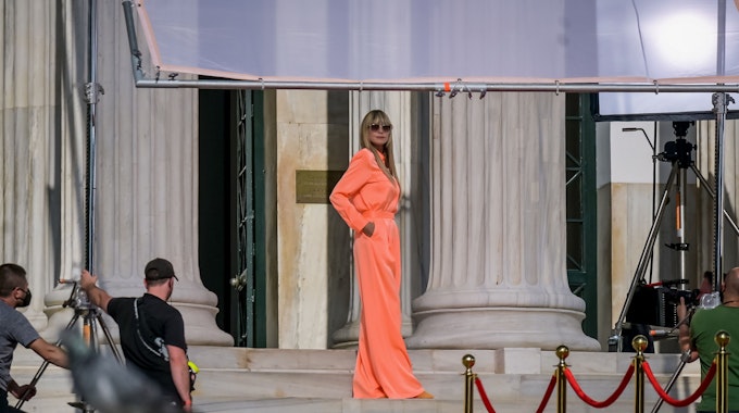 Heidi Klum posiert auf einem Foto vom 05. November 2021 in einem orange-farbigen Kleid am Eingang der Zappeion-Halle während der Dreharbeiten für „Germany's Next Topmodel“.