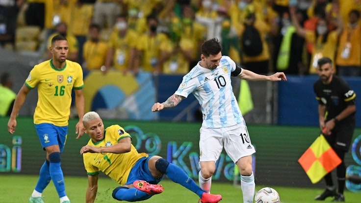 Richarlison aus Brasilien versucht Lionel Messi aus Argentinien zu stoppen, während Renan Lodi zuschaut.