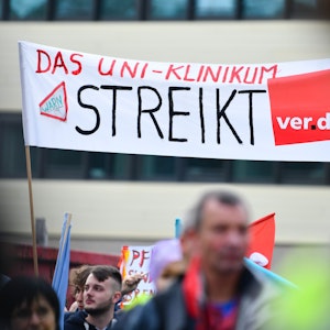 Streikende Beschäftigte halten ein Transparent mit der Aufschrift „Das Uni-Klinikum streikt“ in die Höhe
