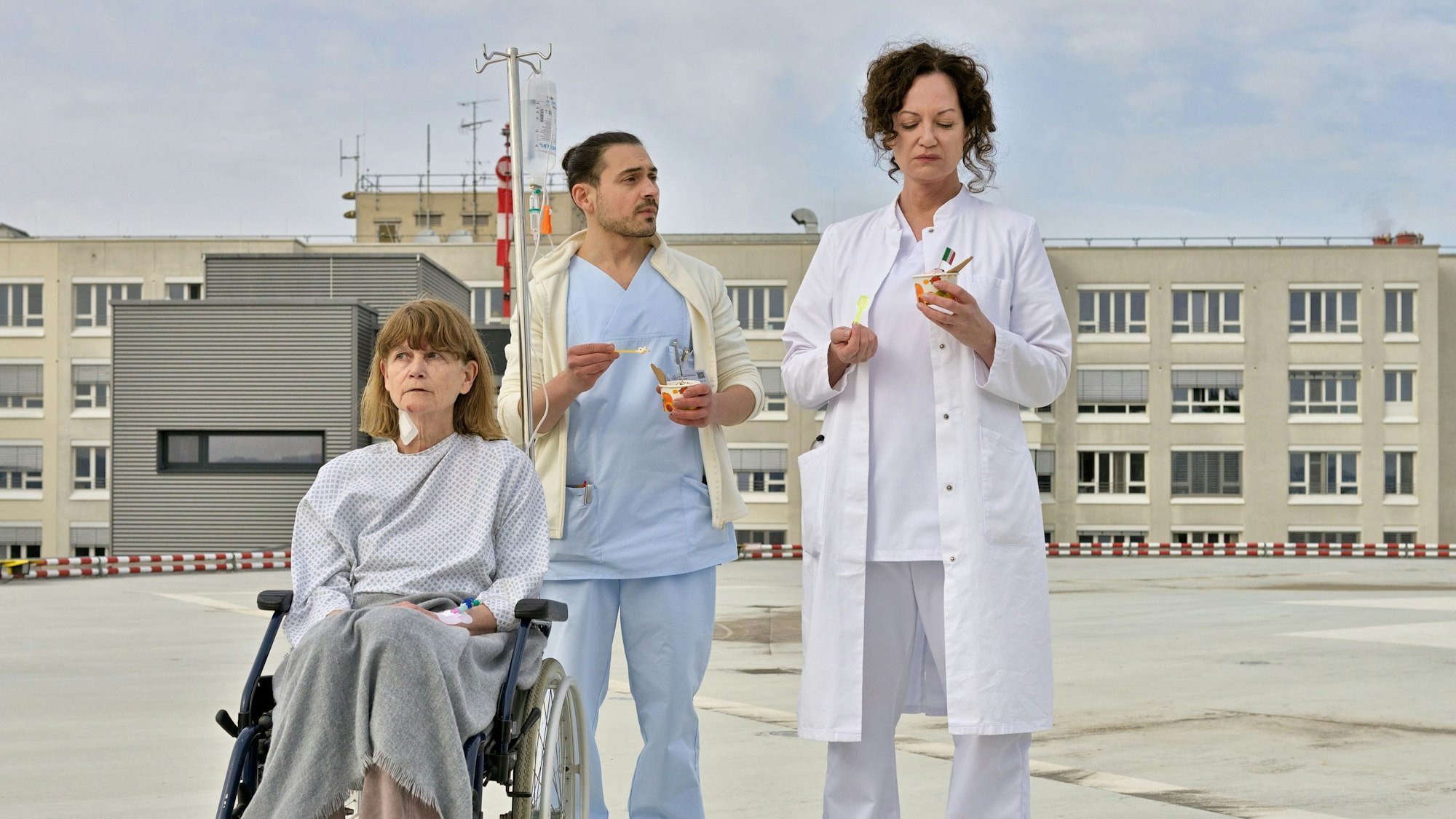 Carolin Mellau (Natalia Wörner, r) und der Pfleger Mirko (Johannes Klaußner) sind mit Madame Laurent (Ursula Andermatt) auf dem Dach der Klinik und essen Eis in einer Szene des Films „Die Welt steht still“ (undatierte Filmszene).