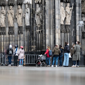 Besucher stehen vor dem Kölner Dom Haupteingang an, am Eingang steht ein sogenannter Domschweizer, eine Aufsichtsperson, aufgenommen am 13. März 2021.