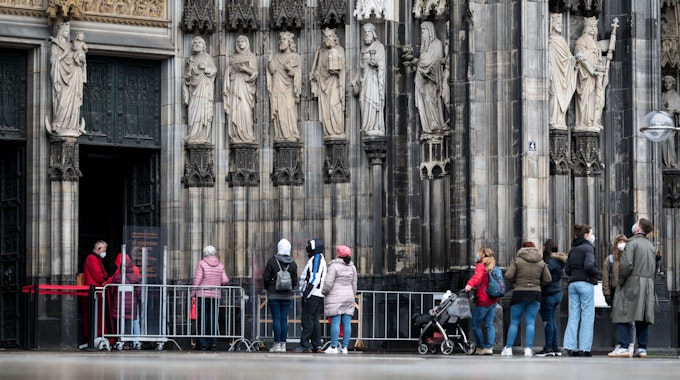 Besucher stehen vor dem Kölner Dom Haupteingang an, am Eingang steht ein sogenannter Domschweizer, eine Aufsichtsperson, aufgenommen am 13. März 2021.