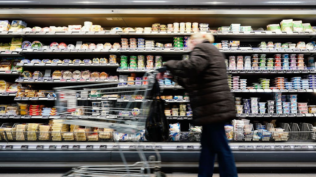 Eine Kundin fährt in einem Supermarkt mit einem Einkaufswagen an einem Lebensmittelregal vorbei.&nbsp;