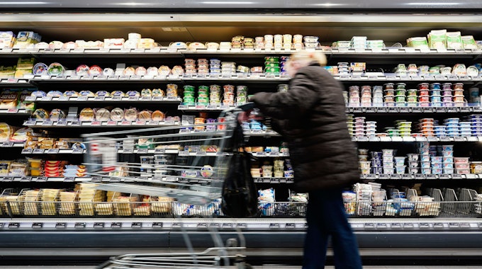 Eine Kundin fährt in einem Supermarkt mit einem Einkaufswagen an einem Lebensmittelregal vorbei.