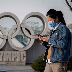 Eine asiatische Frau läuft an der Skulptur der Olympischen Ringe vor dem Nationalstadion „Vogelnest“ in Peking vorbei