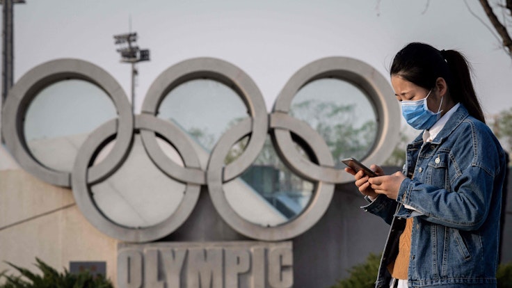 Eine asiatische Frau läuft an der Skulptur der Olympischen Ringe vor dem Nationalstadion „Vogelnest“ in Peking vorbei