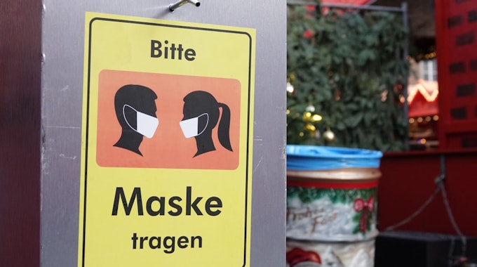 Auf einem Desinfektionsmittelspender am Düsseldorfer Weihnachtsmarkt hängt ein Schild mit der Aufschrift «Bitte Maske tragen».