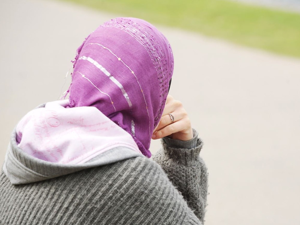 Eine junge Frau mit Kopftuch sitzt an einem Weg.