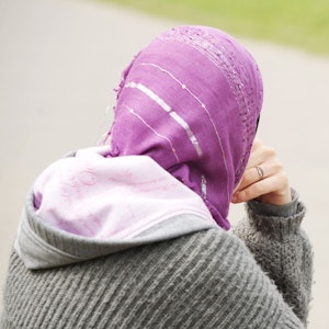 Eine junge Frau mit Kopftuch sitzt an einem Weg.